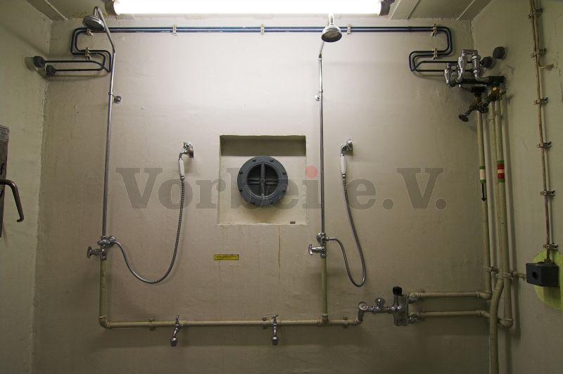 Die Dusche (Raum 56) ist mit 2 Duschvorrichtungen und einer zentralen Mischbatterie ausgestattet. Im linken Bildrand befindet sich der Bedienhebel einer weiteren Kleiderrutsche.