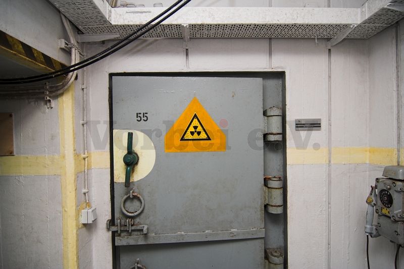 Der Zugang zum Lagerraum für kontaminierte Kleidung (Raum 55) befindet sich in der Zugangsschleuse (Raum 52). Ein Warnschild weist auf eine Strahlungsbelastung hin, die bei der Einlagerung kontaminierter Kleidung auftreten könnte.