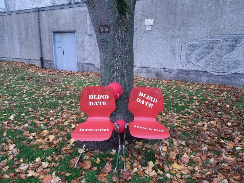 Auf dem Bild sind zwei rote Stühle abgebildet. Die Stühle sind mit "Blind Date Kultur" beschriftet und sind das Erkennungszeichen der Veranstaltungsreihe. Sie wurden vor dem Bunker aufgestellt.