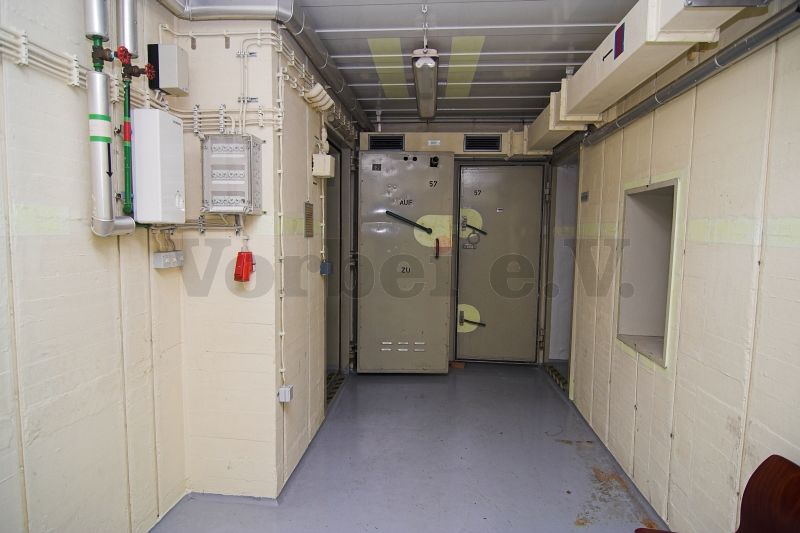 Blick in den Raum 57: Die linke Tür führt in Duschraum (Raum 56) und die rechte Tür in das WC Ankleideraum (Raum 58). Auf der rechten Wand befindet sich die Durchreiche für saubere Kleidung, die in den Raum 59 (Lagerraum für saubere Bekleidung) führt.