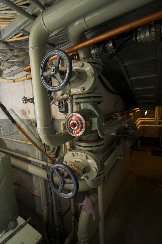 Eine Umwälzpumpe sitzt zwischen zwei Absperrventilen im Museumsbunker Hannover. Rohrleitungen führen zu einem Deckendurchbruch. Dort ist der Kühler platziert, zu dem das Kühlwasser mit der Umwälzpumpe befördert wird.