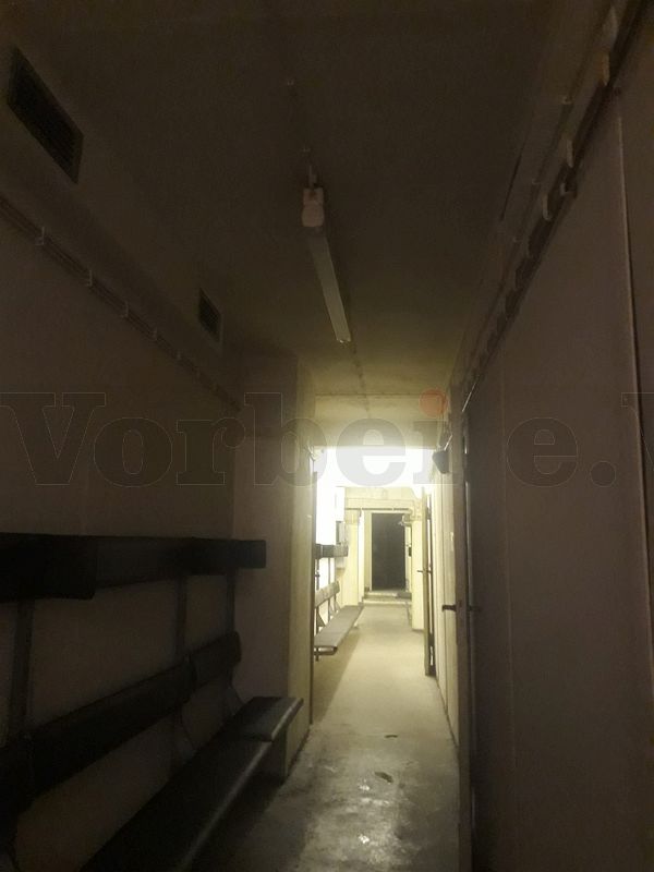 In einem Durchgangsflur im Museumsbunker ist eine Deckenlampe defekt. Auf der rechten Seite des Durchganges befinden sich Schutzraum-Sitzbänke. Aufgrund der defekten Lampe wird dieser Bereich nicht mehr ausreichend ausgeleuchtet.