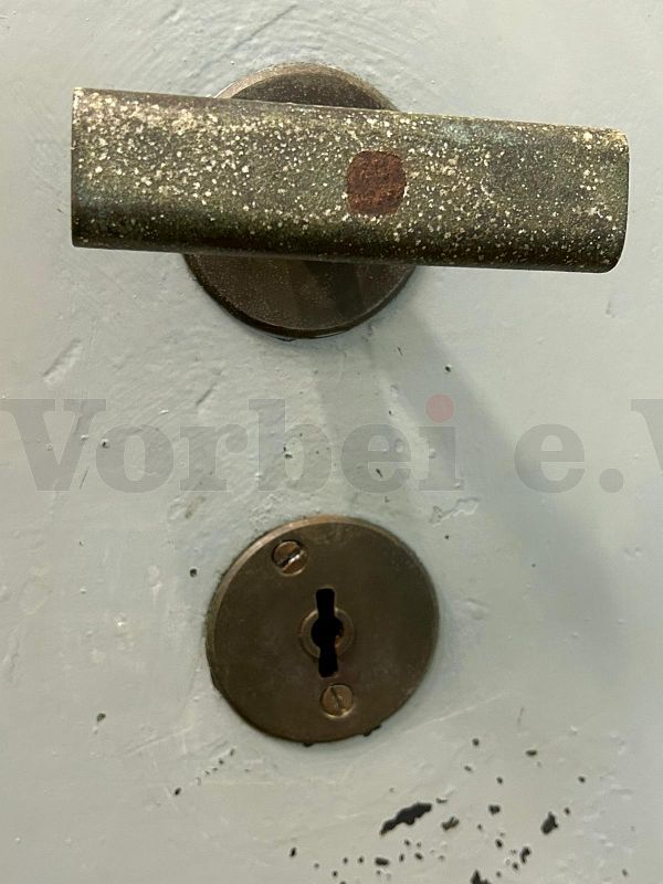 Die Detailaufnahme der Schließvorrichtung zeigt, dass die Schlüsselöffnung auf der Tür direkt zugänglich ist und nicht durch eine Abdeckung verdeckt wird. Über dem Schlüsselloch befindet sich ein T-förmiger Türgriff.
