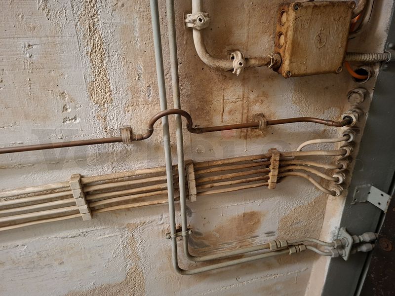 Detailansicht: Die Messleitung des Manometers führt in einem Bogen über die beiden Hydraulikleitungen und dann weiter durch die druckdichte Wanddurchführung in den Schleusenbereich. Detailansicht: Die Messleitung des Manometers führt in einem Bogen über die beiden Hydraulikleitungen und dann weiter durch die druckdichte Wanddurchführung in den Schleusenbereich.