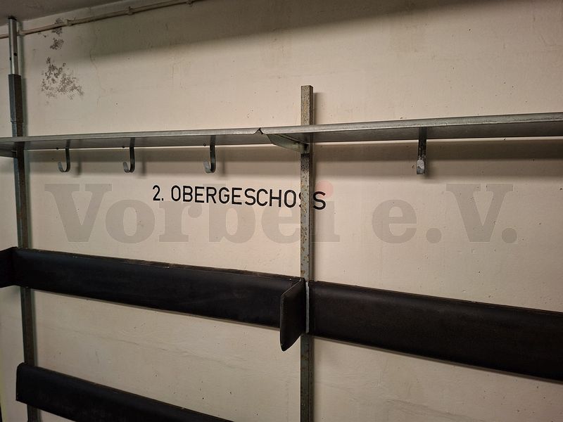 Hinter einer Sitzbankreihe befindet sich die Wandbeschriftung &bdquo;2. Obergeschoss&ldquo;.