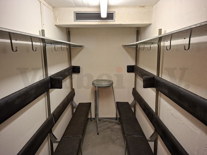 Ausstattung einer kleinen Nische im Treppenbereich des zweiten Obergeschosses mit Schutzraum-Sitzbänken und einem Abfallbehälter.