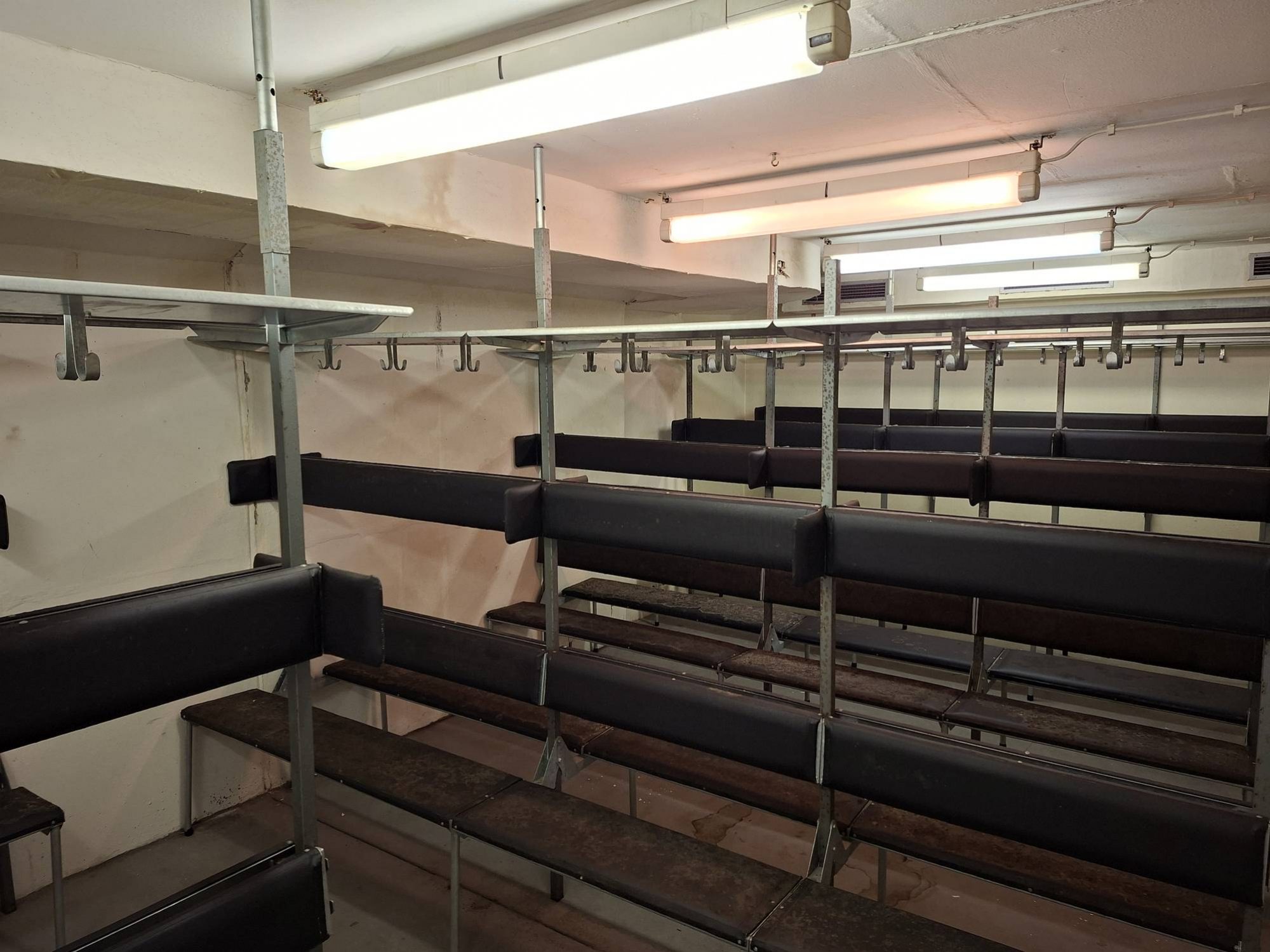 Ein mit Schutzraum-Sitzbänken ausgestatteter Schutzraum im zweiten Obergeschoss des Museumsbunkers Hannover. Diese Ebene sowie das darüberliegende dritte Obergeschoss konnten aufgrund von Wasserschäden wegen einer undichten Dacheindeckung über einen langen Zeitraum nicht genutzt werden. Erst nach einer gründlichen Überprüfung der betroffenen Bereiche konnten wir die Stromversorgung vor kurzem wieder in Betrieb nehmen. Damit sind diese Teile des Bauwerks nach langer Zeit wieder zugänglich und können nun schrittweise weiter saniert werden.
